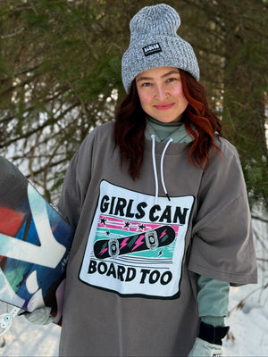 Person wearing oversized tshirt with 'Girls Can Board Too' text in a snowy outdoor setting