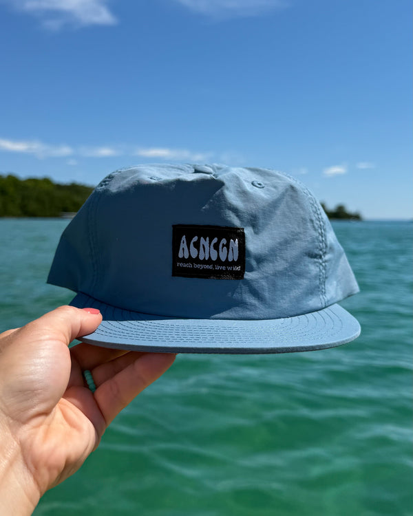 Blue cap held by a hand with a clear blue sky and ocean background