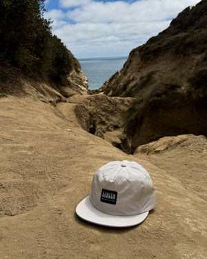 White cap with a logo on a sandy beach with ocean and cliffs in the background